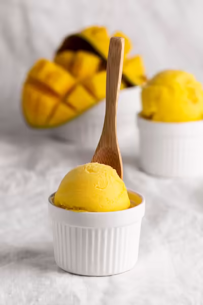 Scoop of bright yellow mango sorbet in a white ramekin with a wooden spoon— a light, pregnancy-friendly dessert for expecting moms.