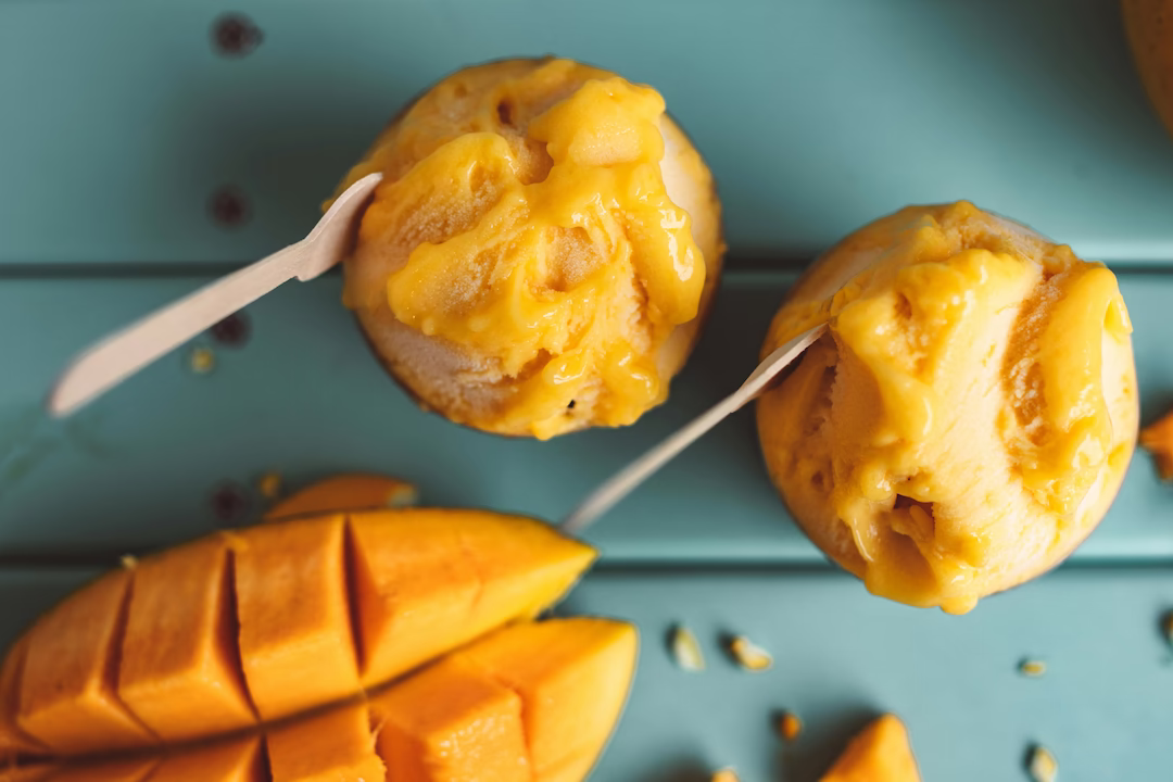 Pregnancy-safe mango sorbet for expecting moms served in a glass cup with a wooden spoon and fresh mango on the side.